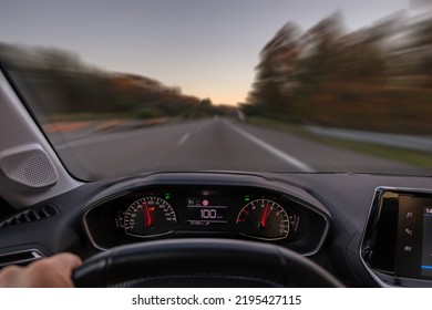 Driver View To The Speedometer At 100 Kmh Or 100 Mph And The Road Blurred In Motion, Night Fall View From Inside A Car Of Driver POV Of The Road Landscape.