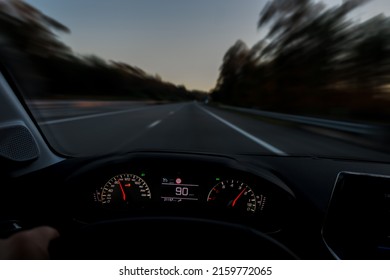 Driver view to the speedometer at 90 kmh or 90 mph and the road blurred in motion, night fall view from inside a car of driver POV of the road landscape.