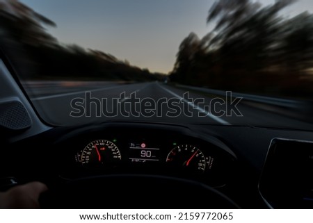 Driver view to the speedometer at 90 kmh or 90 mph and the road blurred in motion, night fall view from inside a car of driver POV of the road landscape.
