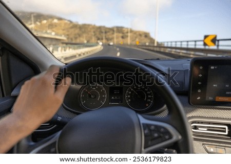 Driver view to the speedometer, with hand on the steering wheel. Blurred road bridge. Madeira island, Portugal.