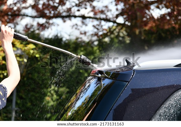 A driver washes a black car with a high-pressure\
water jet at his home.