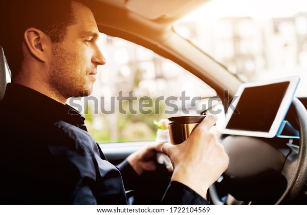 The driver watches movies or TV shows on\
the tablet during lunch. Stopping for a bite to eat . Man eat snack\
in the car and drinks coffee or\
tea.