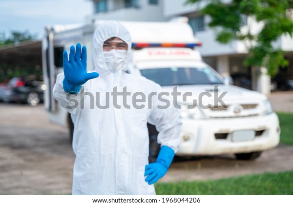 Driver wear PPE in front of the ambulance\
with protective suit at ambulance car vehicle for helping the\
patient of Coronavirus or Covid-19, Hand indication of stopping the\
spread of the\
coronavirus