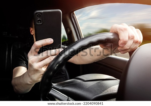 The driver at the wheel of a car uses a smartphone,\
distracted from the road.