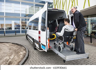 The Driver Of A Wheel Chair Taxi, Helping A Disabled Man In A Wheel Chair, Using The Lift In The Back Of His Mini Van