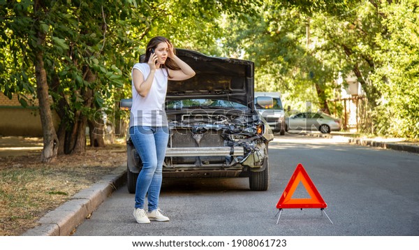 Driver woman in front of wrecked car in car\
accident. Scared woman in stress holding her head after auto crash\
calling to auto insurance for help. Dangerous road traffic\
situation. Long web\
banner
