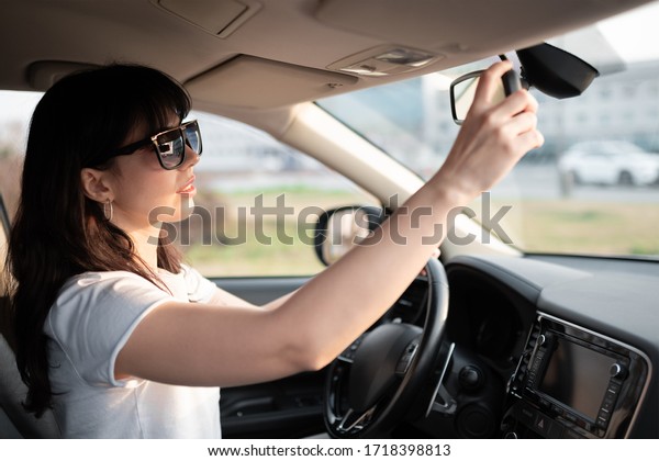 Driver\
woman try to correct rearview mirror inside her car. Safety driving\
concept. Woman prepearing to drive reversive.\

