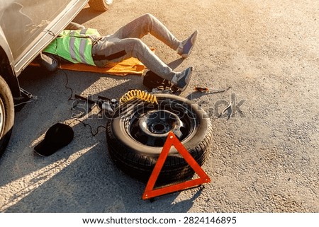 A driver or worker repairs a broken car on the side of the road. View from above. Man is under the car.