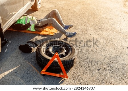 A driver or worker repairs a broken car on the side of the road. View from above. Man is under the car.
