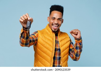 Driver young black man 20s years old wears yellow waistcoat shirt hold in hand new car key doing winner gesture clenching fists say yes isolated on plain pastel light blue background studio portrait