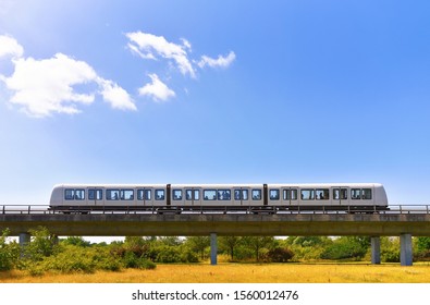 Driverless metro train is moving by overground railroad in countryside area on nature background. Zero emissions of public transport or concept of save environment.