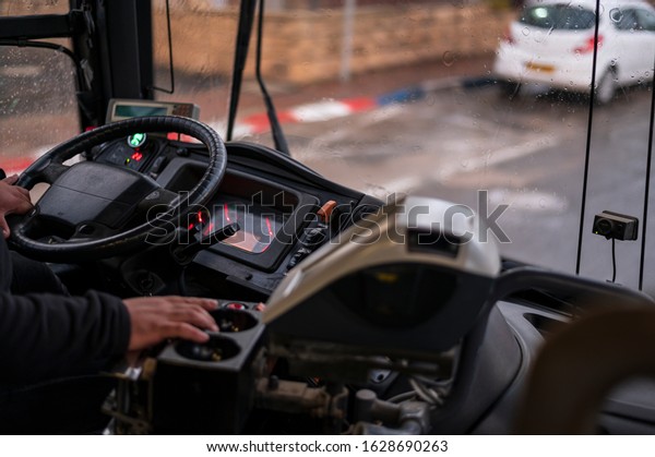 The drivers\
cab of the public bus, his hand on the drivers wheel, outside the\
window - it s rainy.\
Close-up.