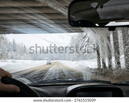Drivers face low visibility through a dirty frozen windshield as they navigate a snowy road under an overpass.