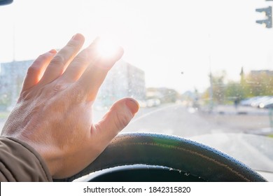 the driver's hand and fingers at the wheel of a moving car cover the sun, which blinds the eyes and does not see the roadway
