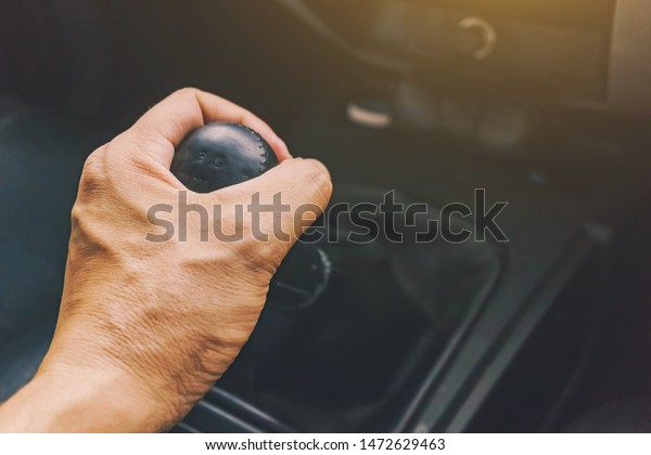 The driver\'s hand is holding the car gear. The\
driver\'s hand grabs the car\'s gearshift and prepares to put it into\
gear to drive the car\
forward.
