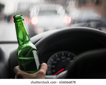 driver's hand holding green beer bottle on road with light bokeh of cars, raining, "drink don't drive" campaign, selective focus