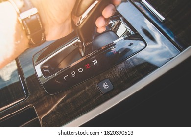 The driver's hand moved the gear selector to the reverse (R) mode of the automatic transmission in the car