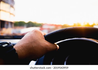 Driver's Hand On The Steering Wheel Inside Of A Car On Road, A Man Driving A Car In City Rush Hour Traffic Congestion Discomfort Drive At Low-speed Morning Sun View.