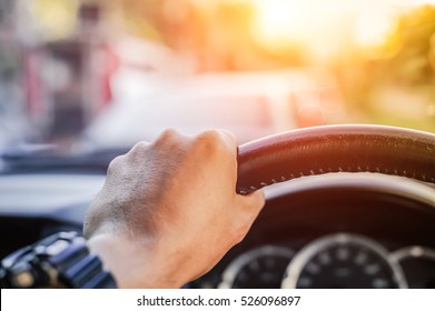 Driver's Hand On The Steering Wheel Inside Of A Car On Road, A Man Driving A Car In City Rush Hour Traffic Congestion Discomfort Drive At Low-speed Morning Sun View.