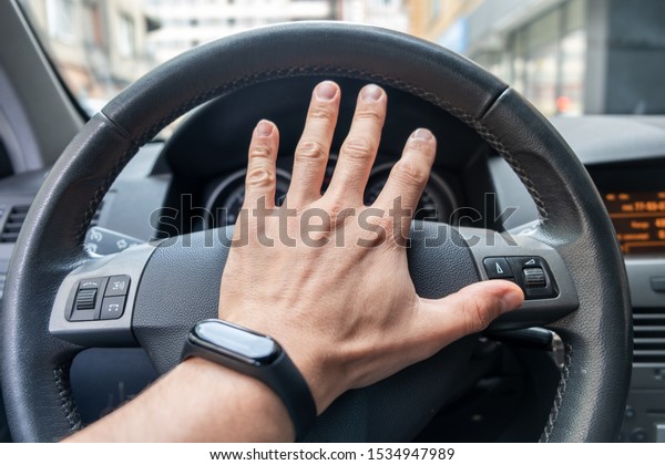 Drivers hand on a\
steering wheel of a\
car.