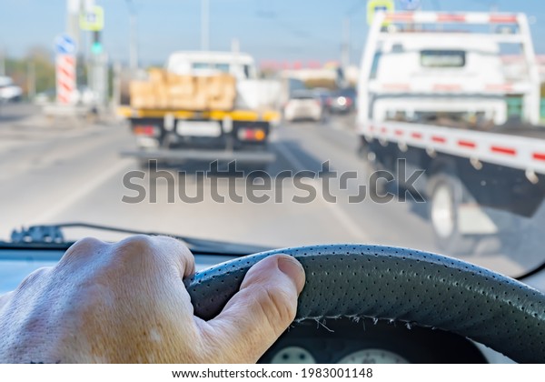the\
driver\'s hand on the steering wheel inside the car during a traffic\
jam in the city traffic flow against the background of two trucks\
in front of a pedestrian crossing and a traffic\
light