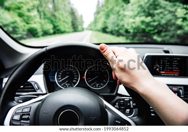 Driver\'s hand on steering wheel on forest\
background. Driving car\
concept.