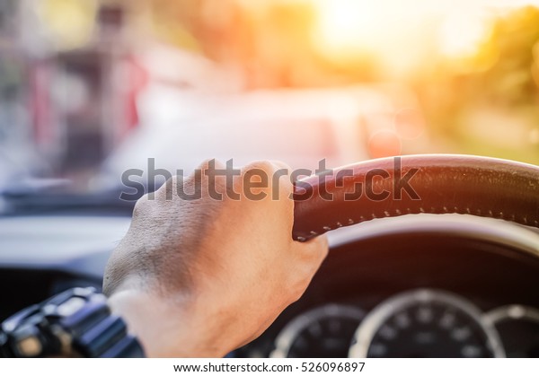 Driver\'s hand on the steering\
wheel inside of a car on road, a man driving a car in city Rush\
hour Traffic congestion Discomfort Drive at low-speed morning sun\
view.