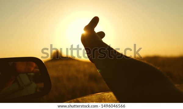 drivers hand is\
playing with sun from car window against beautiful sunset. Girl\'s\
hand waves sun. To travel by\
car