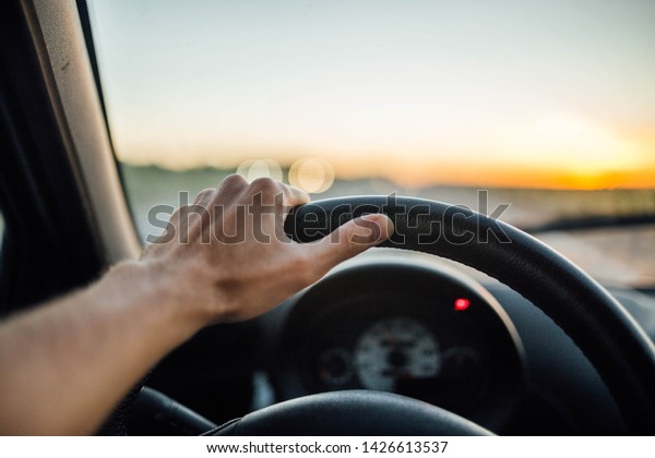 driver\'s hands driving a car on a hot sunny day.\
trip to nature outside the\
city.