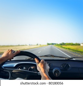 Driver's hands on a steering wheel of a retro car during riding on an empty asphalt road