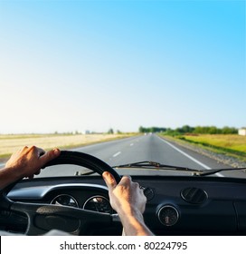 Driver's hands on a steering wheel of a retro car during riding on an empty asphalt road