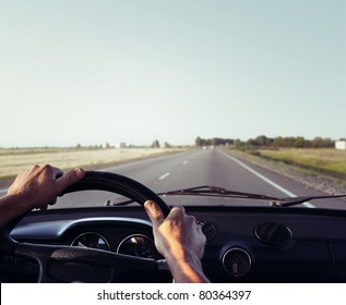 Driver's Hands On A Steering Wheel Of A Retro Car During Riding On An Empty Asphalt Road