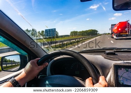 The driver's hands on the steering wheel inside the car when overtaking a tanker truck.