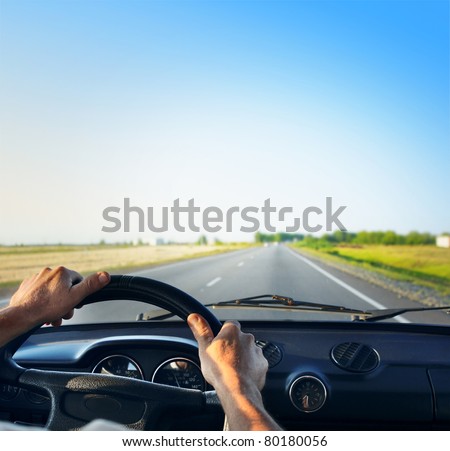 Driver's hands on a steering wheel of a retro car during riding on an empty asphalt road