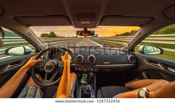 Driver's
hands on a steering wheel of a car and woman in the passenger seat.
Road trip on the Italians road at sunset
time.