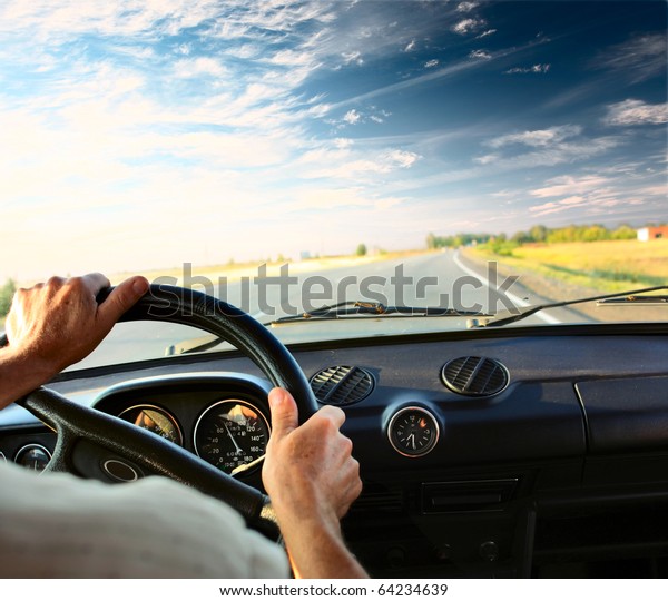 Driver\'s hands on a steering wheel of a car and\
blue sky with clouds