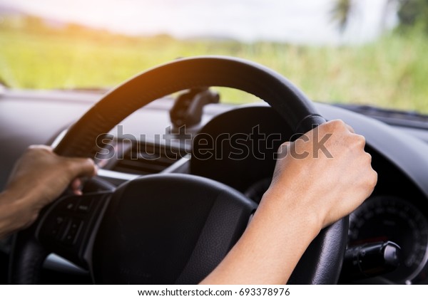 Driver\'s\
hands on the steering wheel inside of a car with beautiful green\
forest perspective, road trip travel\
concepts.