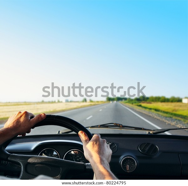Driver\'s hands on a steering wheel of a\
retro car during riding on an empty asphalt\
road