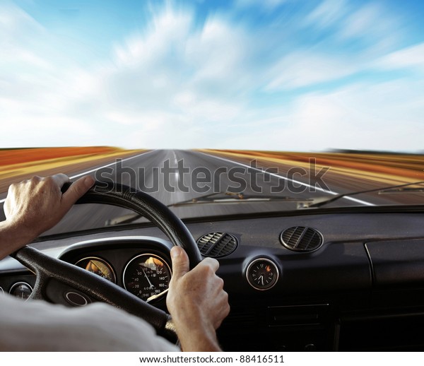 Driver\'s hands on a steering wheel with motion\
blurred road and sky