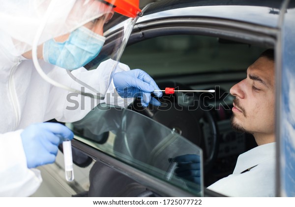 Drive-thru Coronavirus COVID-19 test,paramedic in\
personal protective equipment & face shield performing nasal\
swab through car window on male patient sitting in vehicle,mobile\
US testing site center\
