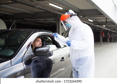 Drive-thru COVID-19 test site,medical staff wearing PPE and face shield performing nasal swabbing,young male driver patient waiting sitting in automobile while worker takes specimen through car window - Powered by Shutterstock