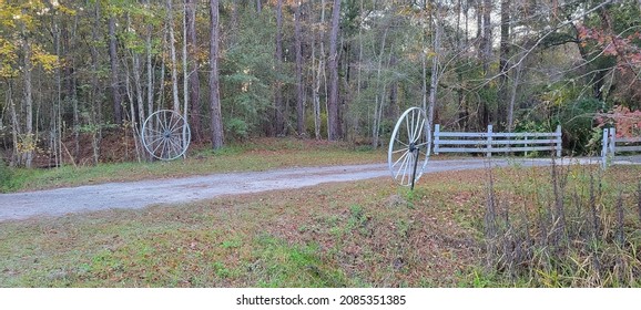 Driveway entrance featuring white vintage wagon wheels dirt road surrounded by dense autumn colored forests in Florida