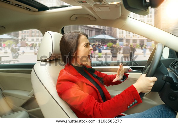 Driving around city. Young attractive woman\
driving a car. Young pretty caucasian model in elegant stylish red\
jacket sitting at modern vehicle interior. Businesswoman concept.\
Human emotions concepts