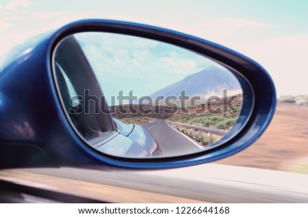 Driving blue car  through side mirror  with reflection of  beautiful Teide volcano  landscape in Tenerife, Canary island,Spain. Concept for travel and adventure.