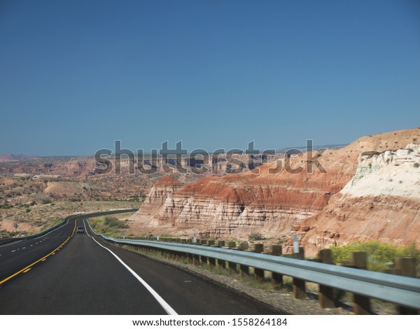 Driving by Arizona lonely desert road, layered red\
rocks on roadsides, black asphalt two lane highway, sunny day,\
clear blue sky, car\
ahead