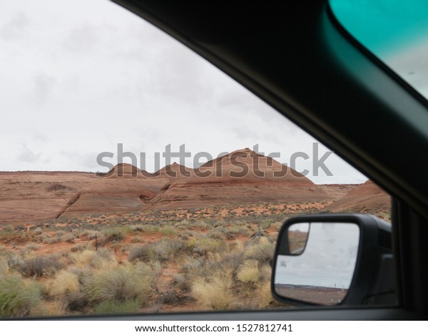 Driving by Arizona red desert landscape,\
scenic view near Lake Powell, cloudy day, red rock strata, layered\
red rock formation in\
foreground