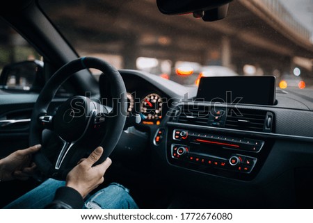 Driving a car in the city. A man driving his modern sports car in the city center. A driver stuck in traffic. Modern car interior with big multimedia screen, sport steering wheel. Driver hold steering
