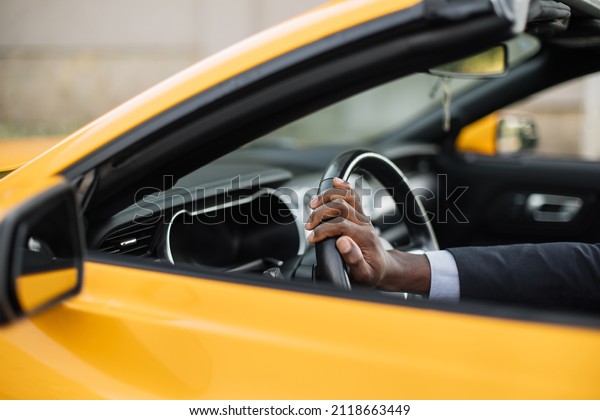 Driving a car. Cropped image of African Men\'s hand\
in business suit holding the steering wheel while driving luxury\
sport car side view.