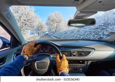 Driving a car - first person shoot. Hands on steering wheel in leather gloves in luxury  car driving on a winter ice road.Panoramic picture.