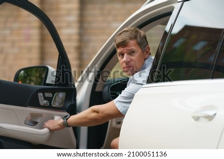 Driving a car. Handsome man opened door of his modern car on the city street. He is blond. He looking into the camera. He is arguing with another car owner on the road. He wrinkled his forehead